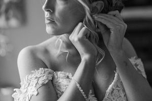 Black and white photo showing someone adjusting a delicate lace wedding dress in dramatic lighting.