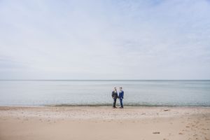 Two people walk together on a vast empty beach under an overcast sky by the ocean.