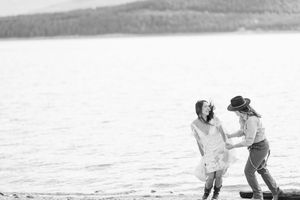 Black and white photo of two people sharing intimate moment by mountain lake.