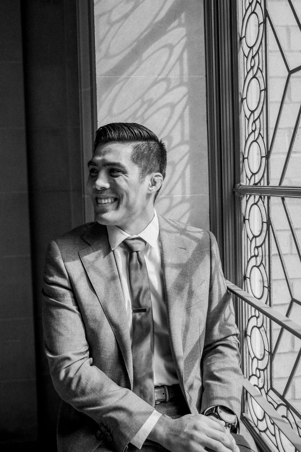 Asian groom sits in beautiful ornate windowsill before eloping at San Francisco City Hall.,