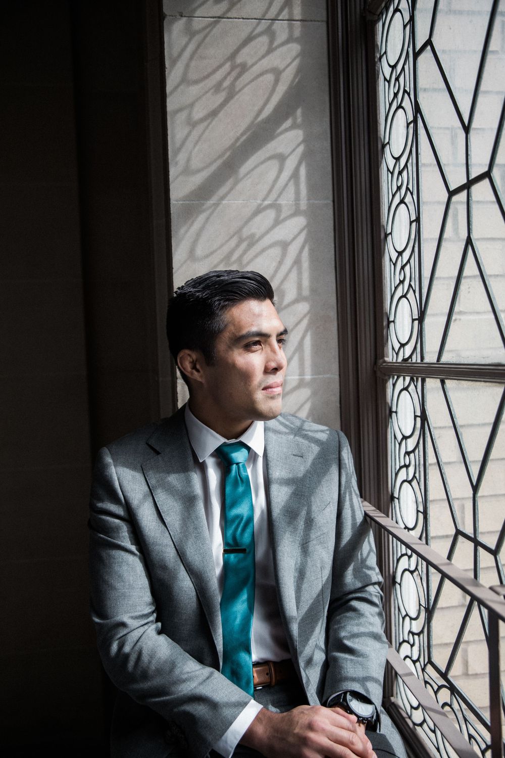 Asian groom sits in beautiful ornate windowsill before eloping at San Francisco City Hall.,