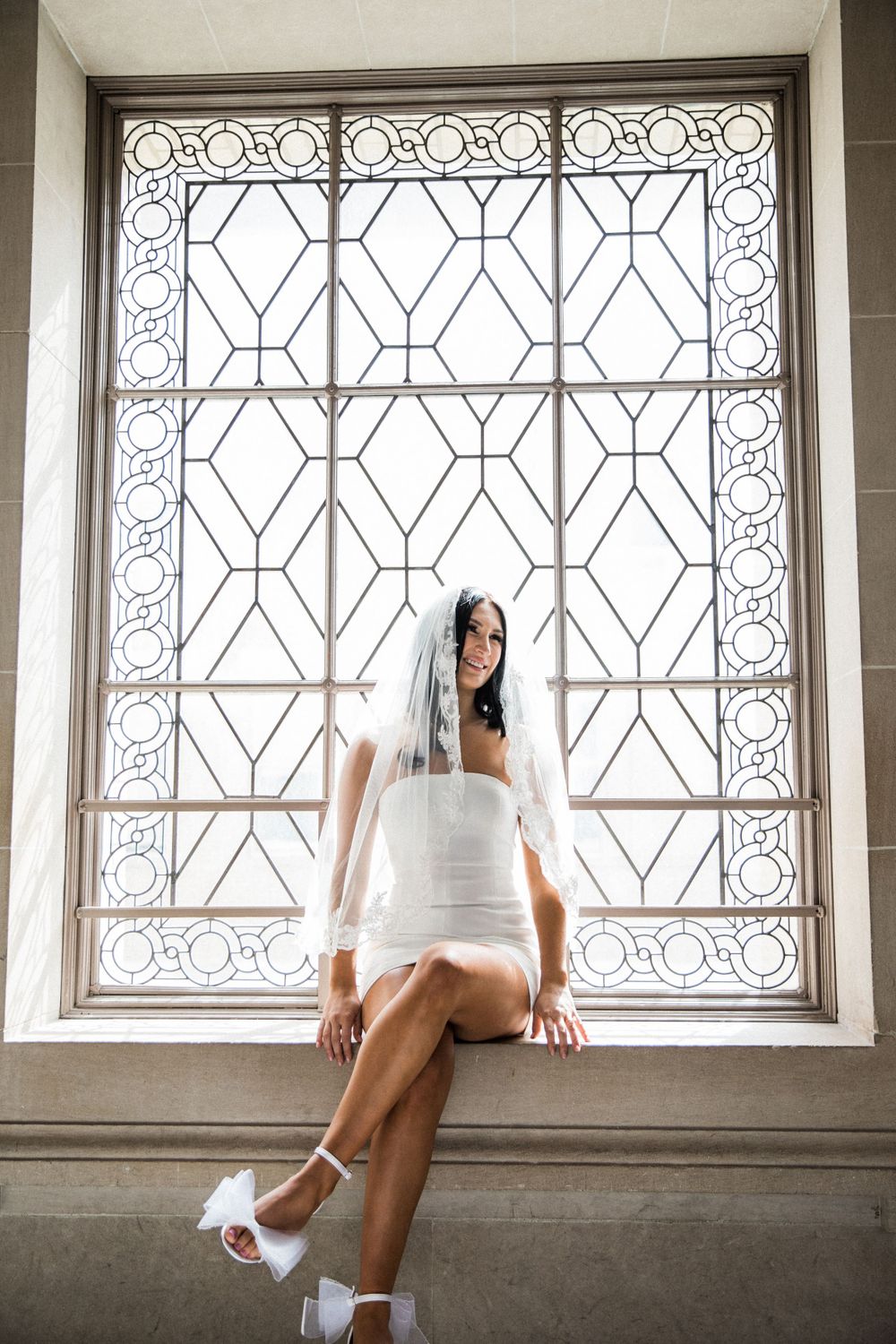 White bride sits in beautiful ornate windowsill before eloping at San Francisco City Hall.,