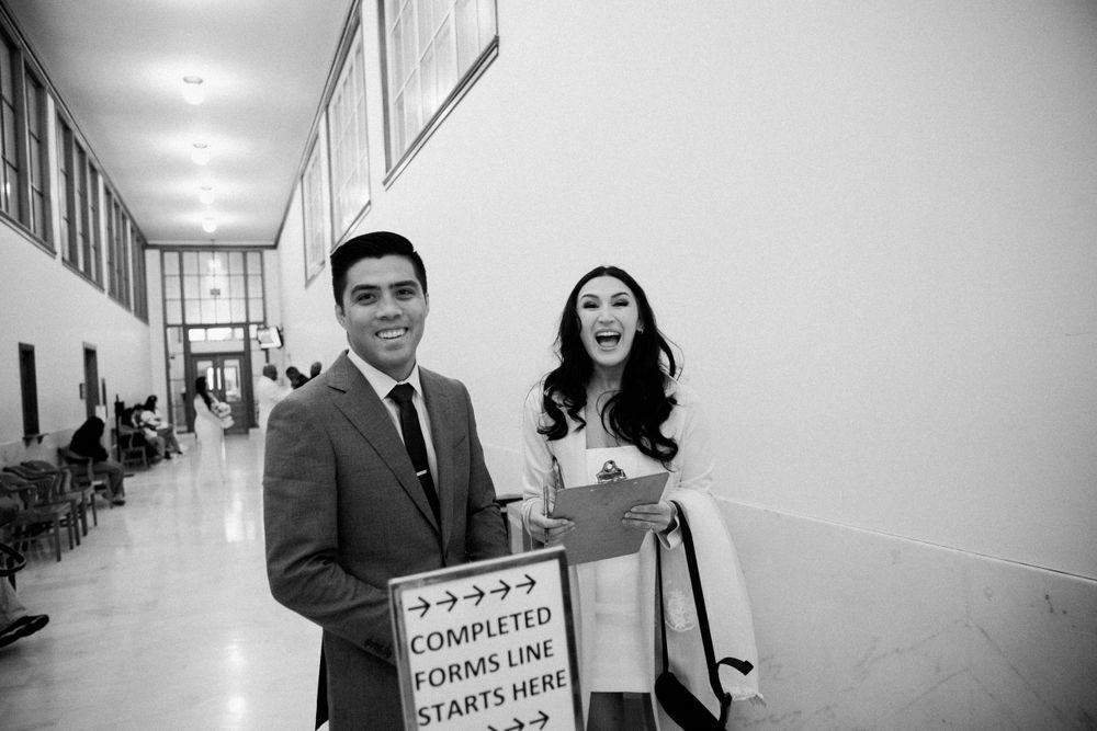 Asian groom and Caucasian bride in short wedding dress smile before getting married at San Francisco City Hall.