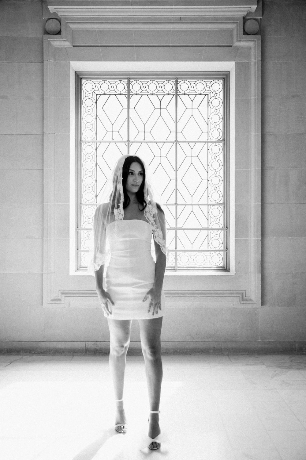 White bride stands  in front of beautiful ornate windowsill before eloping at San Francisco City Hall.,