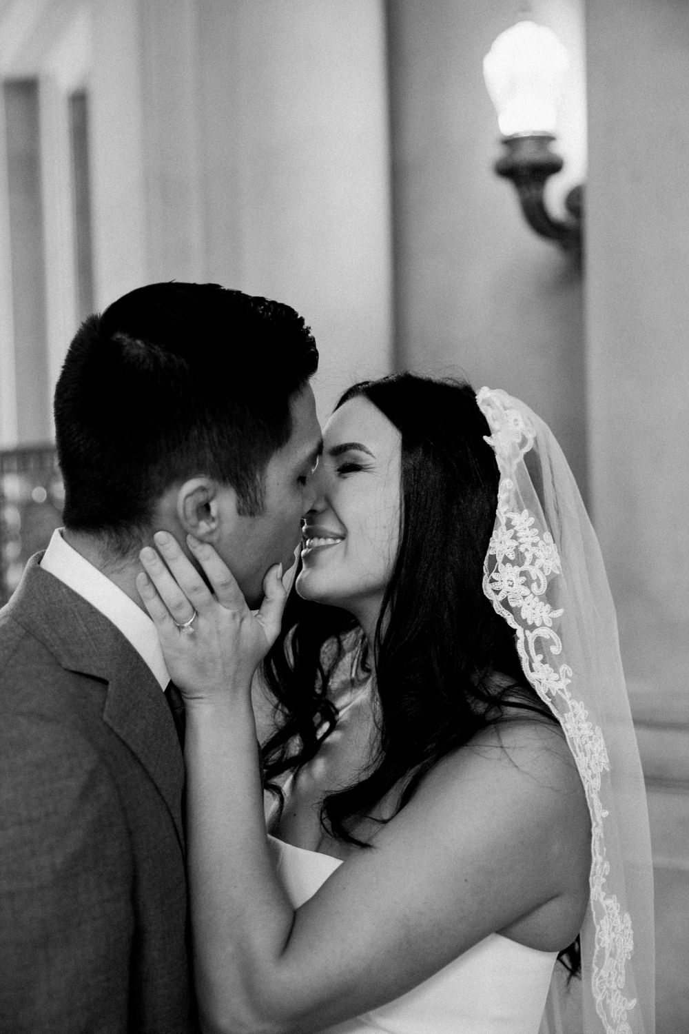 Asian groom and Caucasian bride in short wedding dress kiss after getting married at San Francisco City Hall.