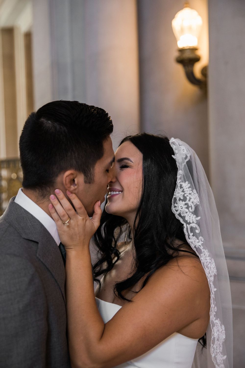 Asian groom and Caucasian bride in short wedding dress kiss after getting married at San Francisco City Hall.