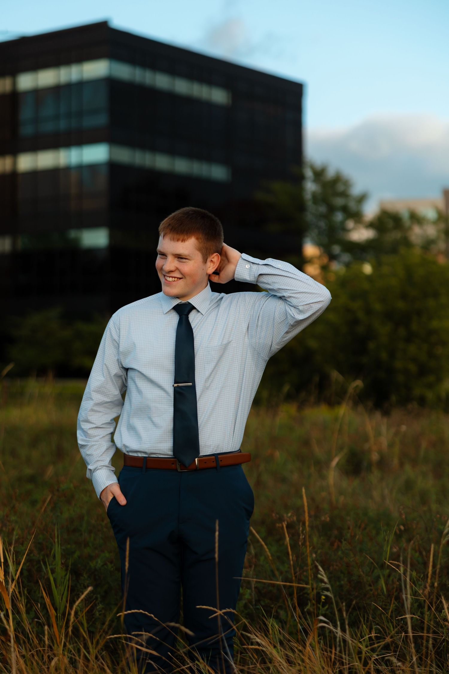 Graduate wearing bright blue cap and gown stands outdoors during golden sunset with bokeh background.