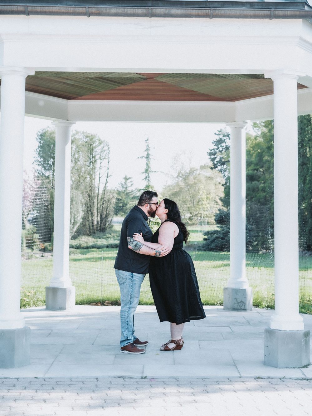 Romantic couple photos taken under a white columned pavilion in a park setting.