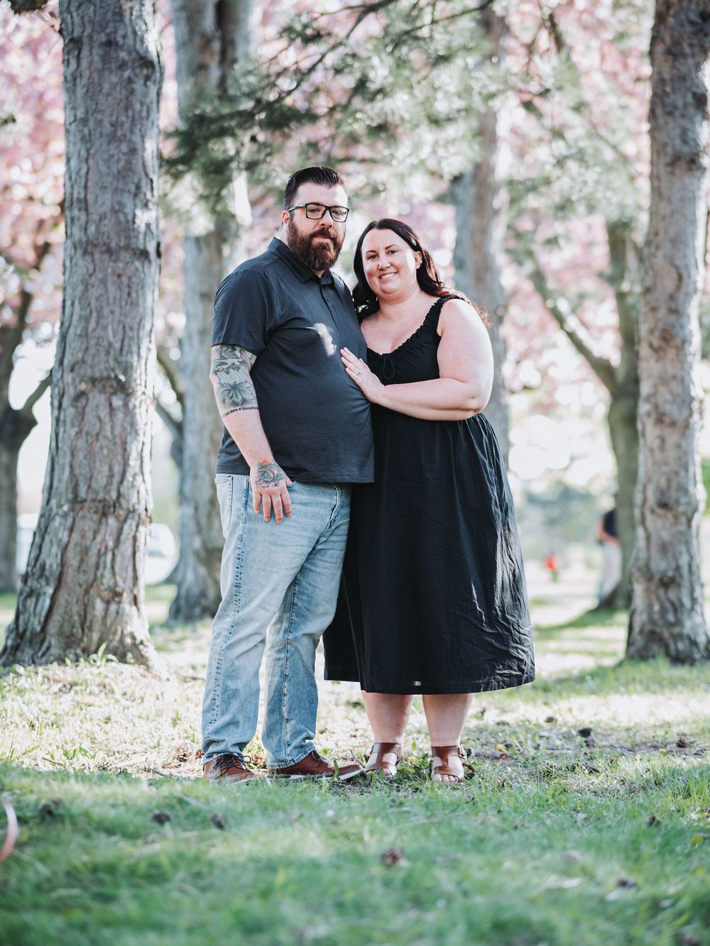A couple standing among cherry blossom trees in a spring garden setting.