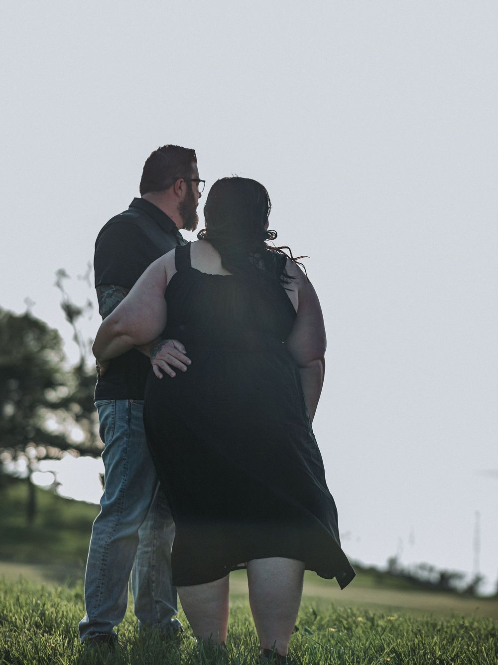 Silhouetted figures embracing on a grassy hillside during golden hour.