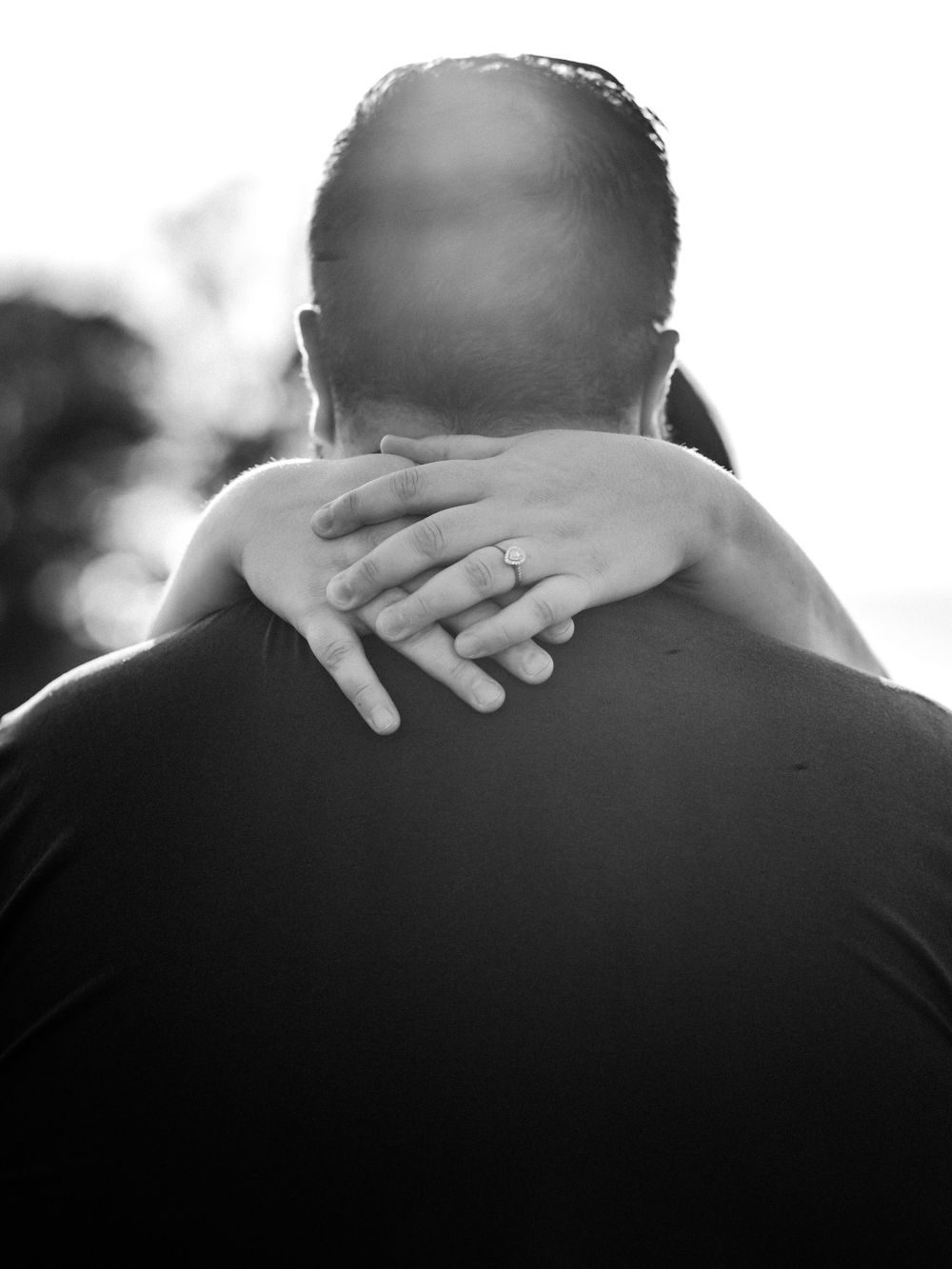 Black and white close-up of hands embracing across shoulders.