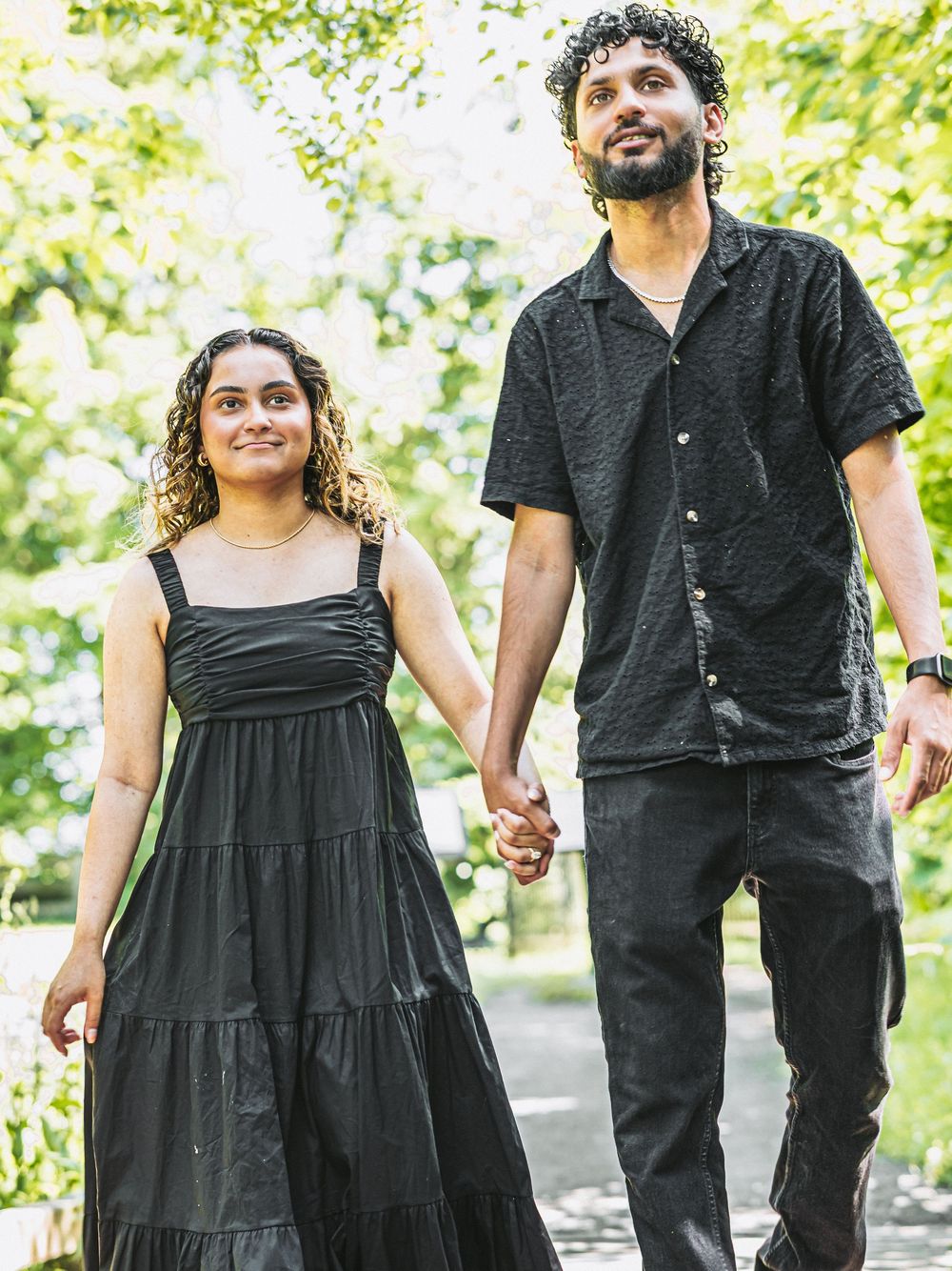 Couple in coordinated black outfits walking together in a sunlit park.