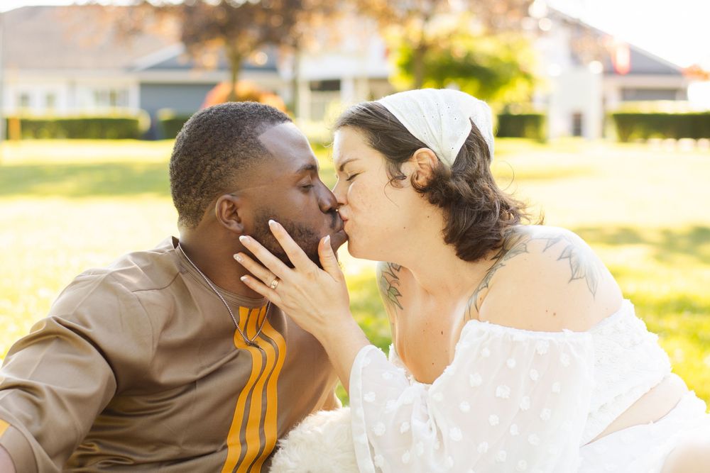 A romantic couple shares a tender kiss in a sunlit garden setting.