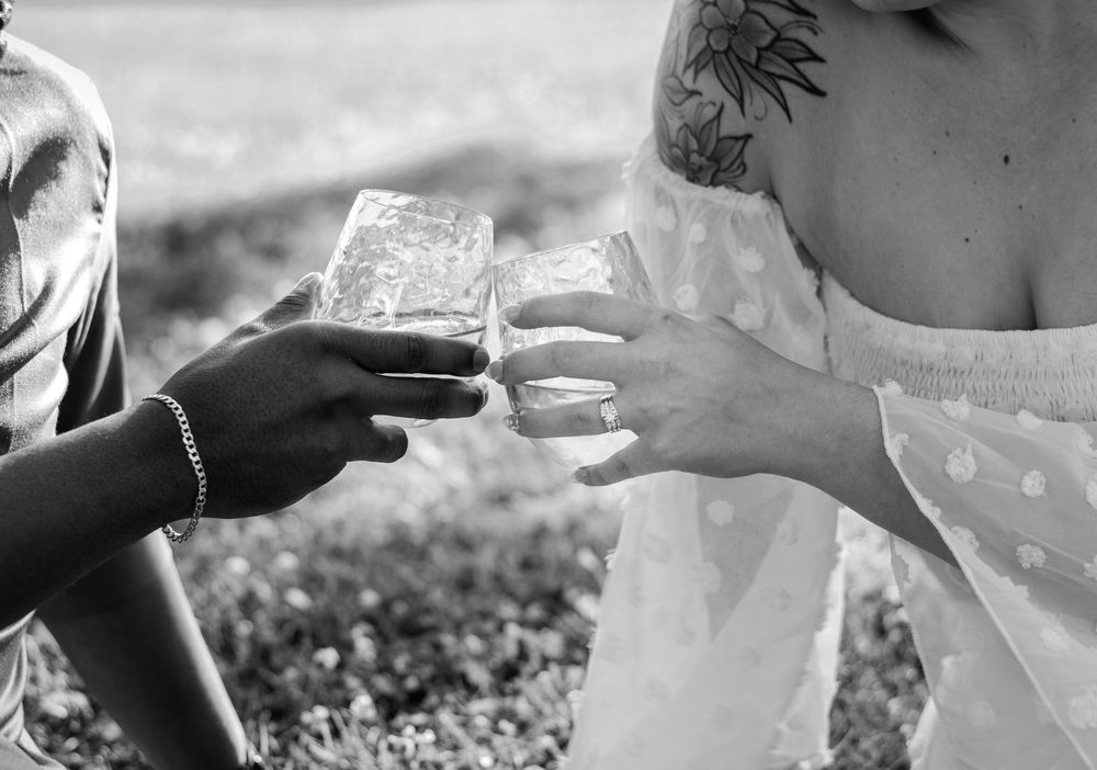Two people clink glasses together in a black and white outdoor setting.