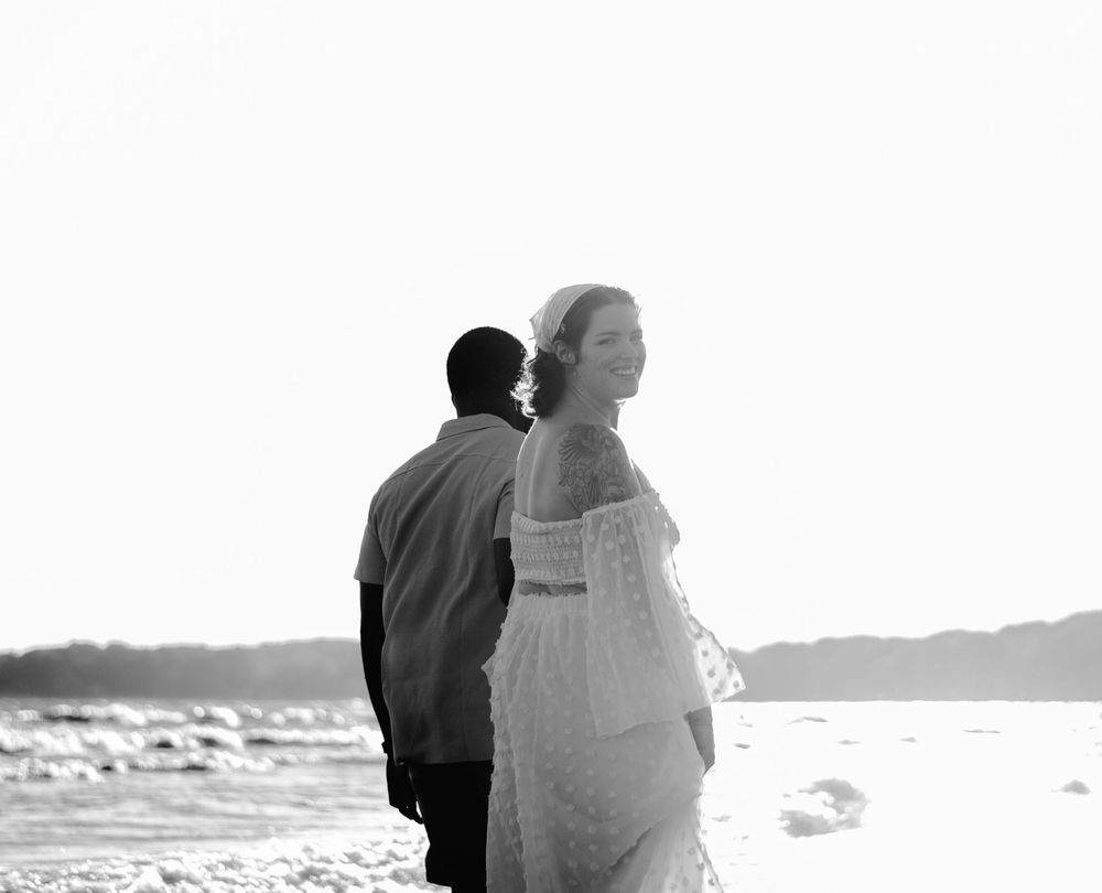 A couple stands together looking out at the ocean during sunset.