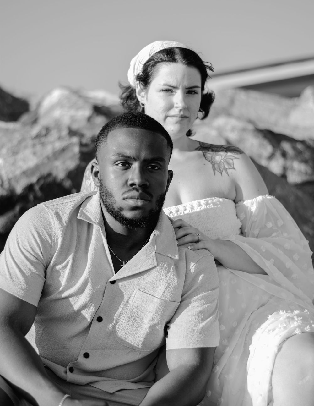 A couple poses for a dramatic black and white portrait on rocky terrain.