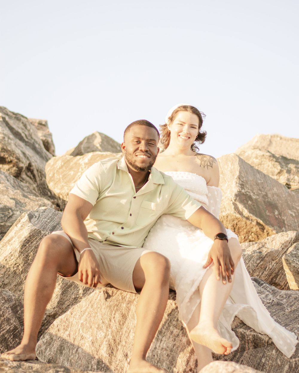 A couple sits together on coastal rocks during a sunny day.