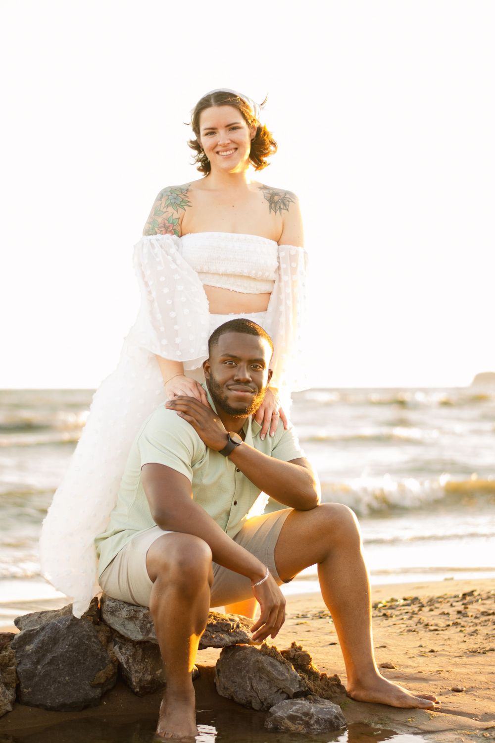 Couple sitting together on rocks at the beach during golden hour.