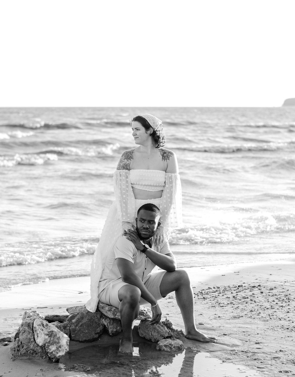 Black and white photo of a couple relaxing on a beach near the waves.