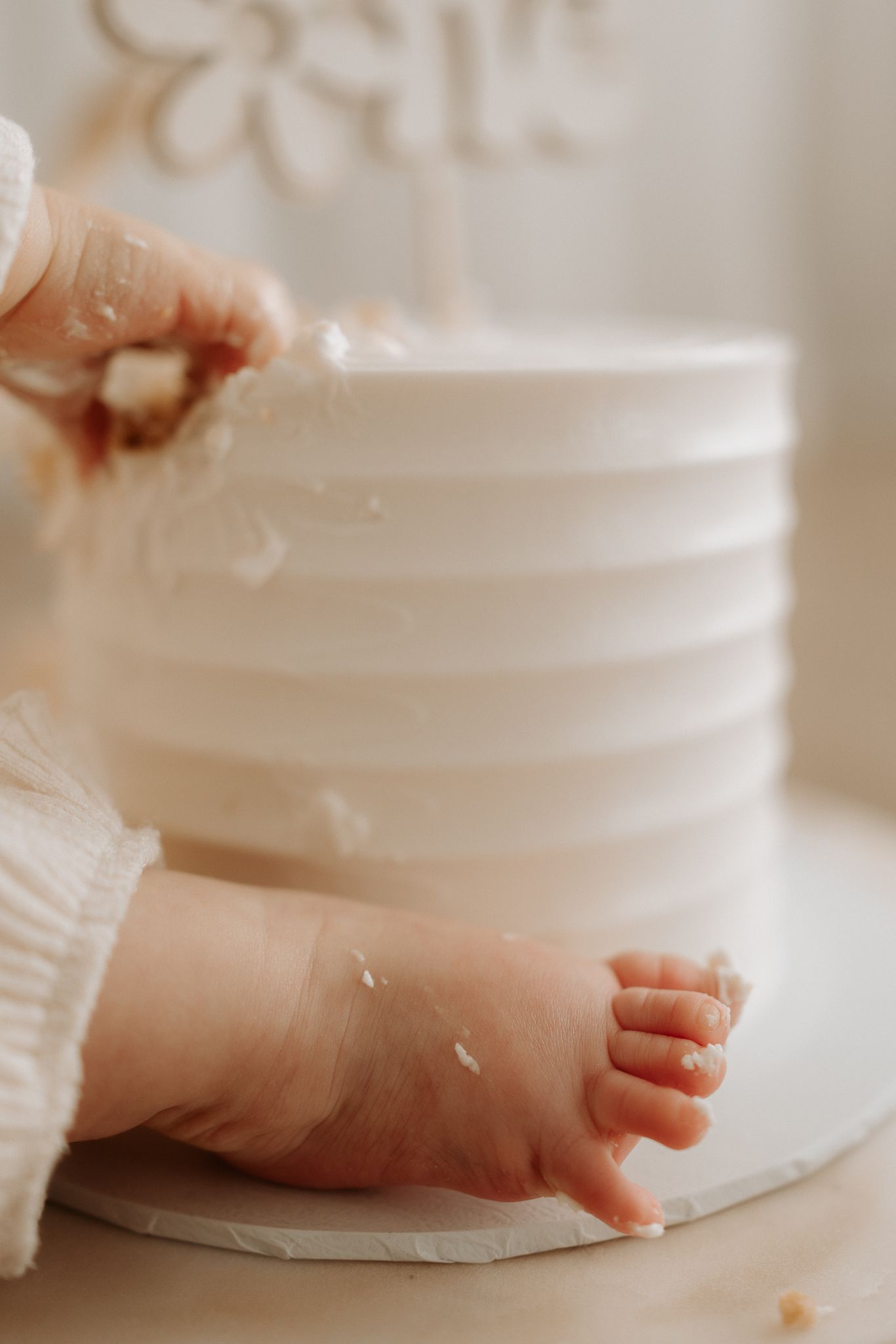 Baby hands and feet touching a white ribbed smash cake during a first birthday celebration.