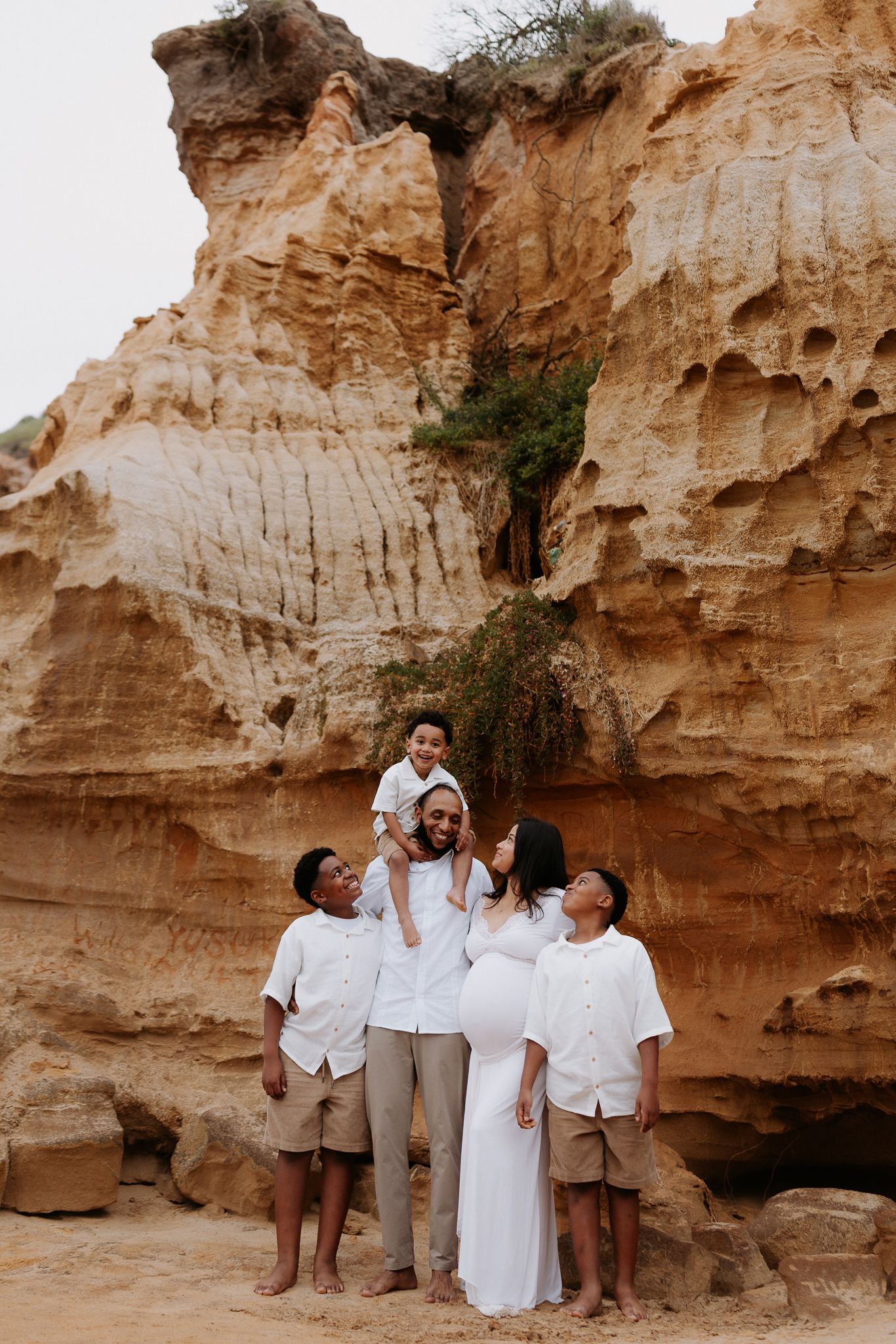 Family of five in white outfits posing before stunning sandstone rock formations in a desert landscape.