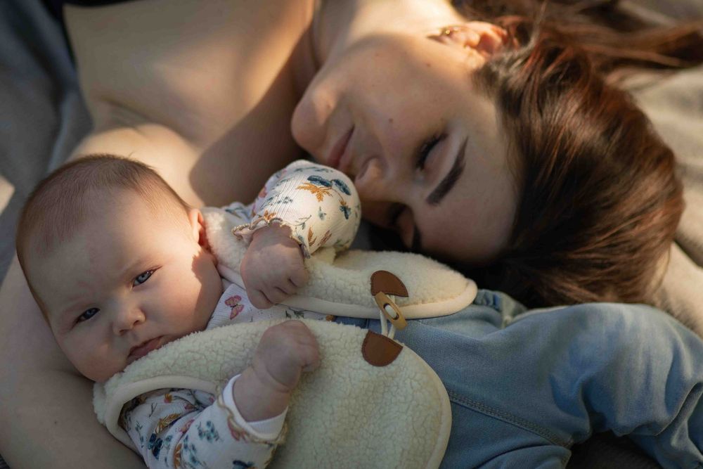 Moeder ligt met haar baby in de armen, liefdevol en ontspannen moment.