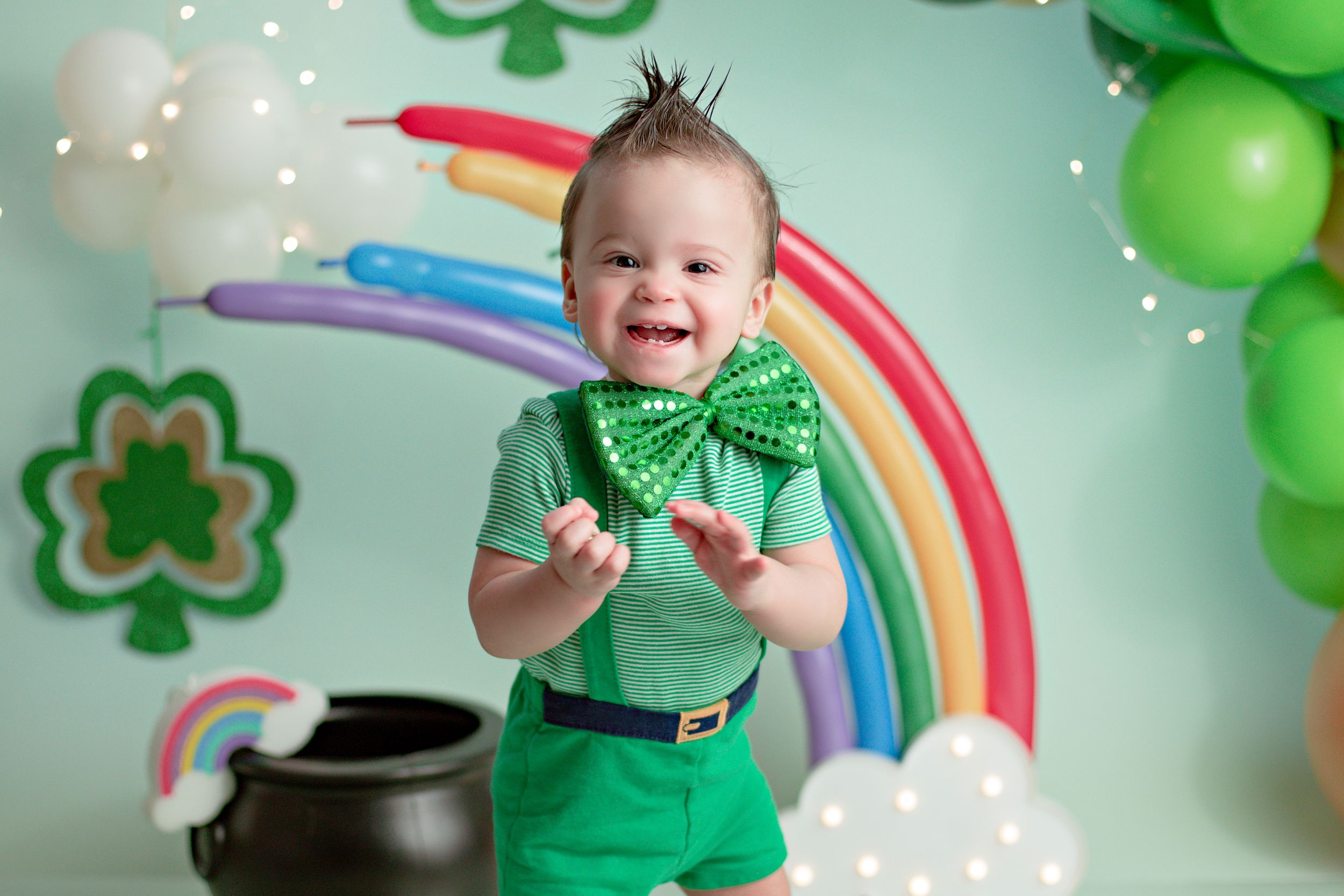Festive St. Patrick's Day setup with rainbow backdrop, shamrocks, and green balloons for holiday photo session.