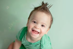 A child in a green shirt smiles brightly against a mint green background.