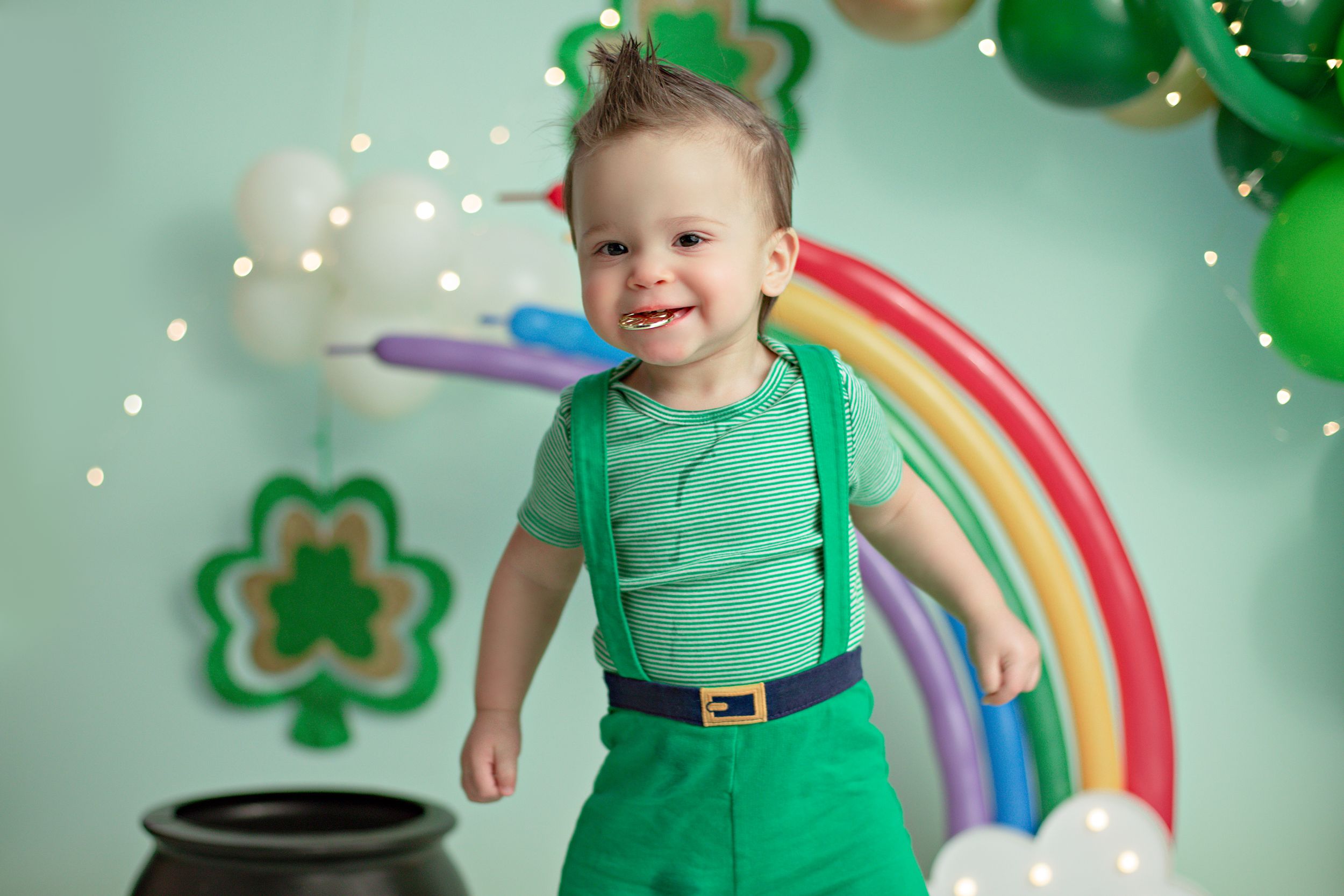 Festive St Patrick's Day themed photo setup with rainbow, green balloons, and pot of gold decorations.