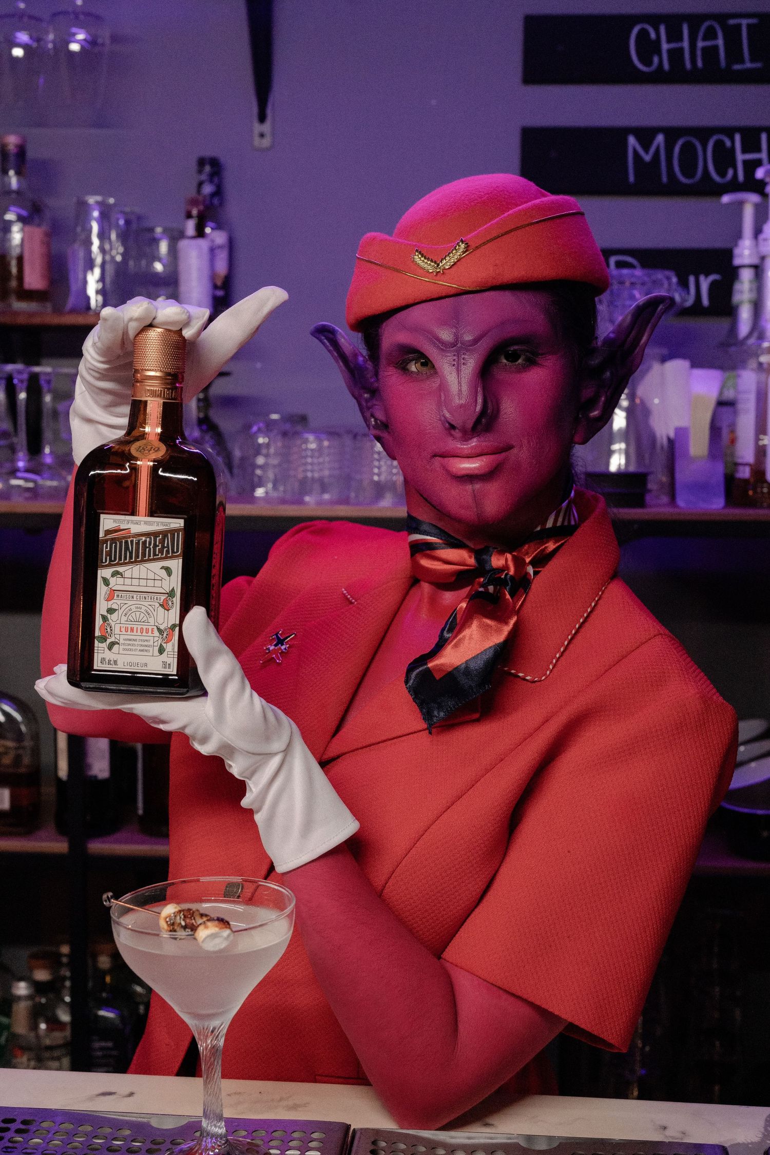 Pink alien dressed like a flight attendant making drinks.