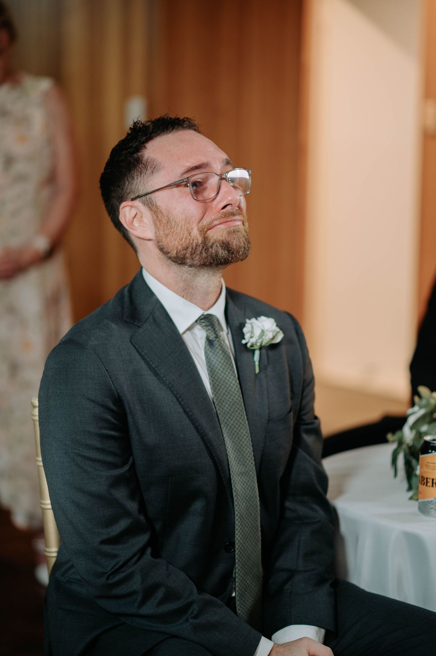 Wedding guest dressed in dark suit and green tie smiling during reception celebration.