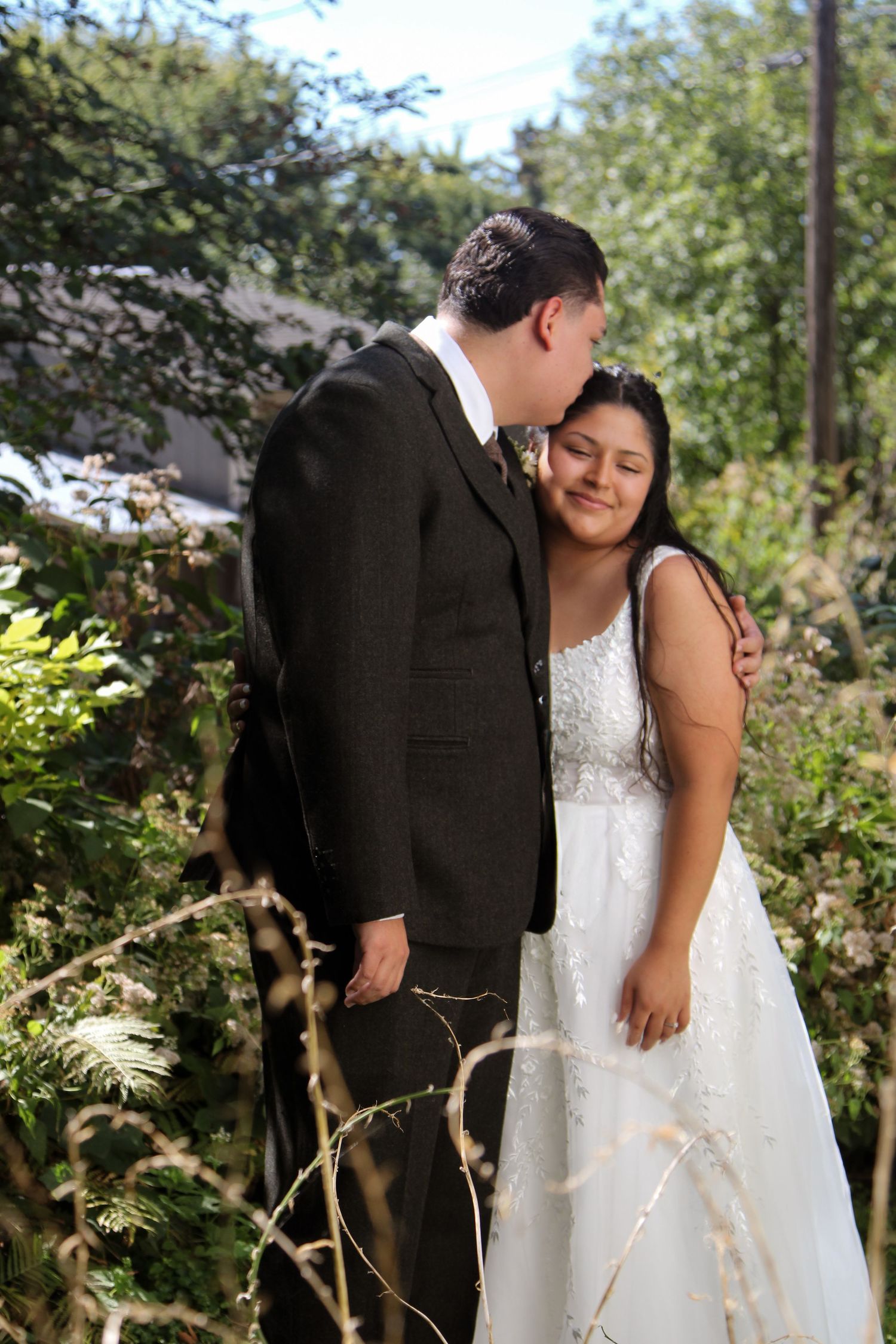 Intimate moment between newlyweds surrounded by lush greenery in a garden setting.