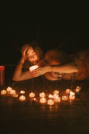 A romantic scene with lit candles on a dark surface while someone glows in candlelight looking at their phone.