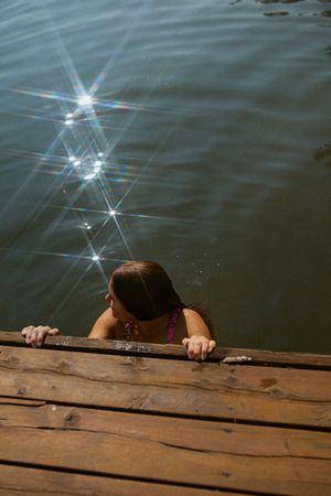 Someone peers over a wooden dock into sparkling water on a sunny day as light dances across the rippling surface.