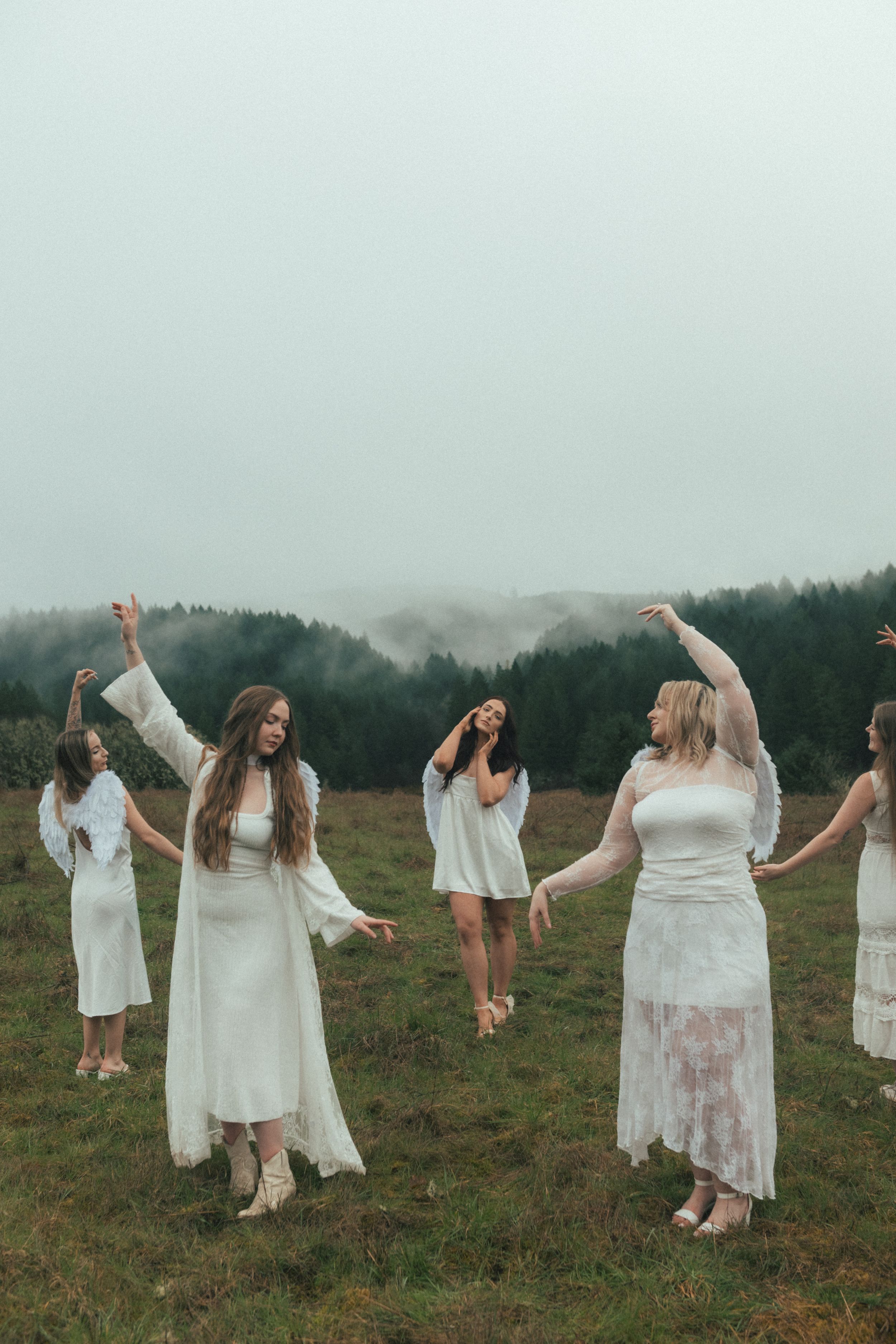 Women in white dresses dancing in a misty field with foggy forest backdrop.