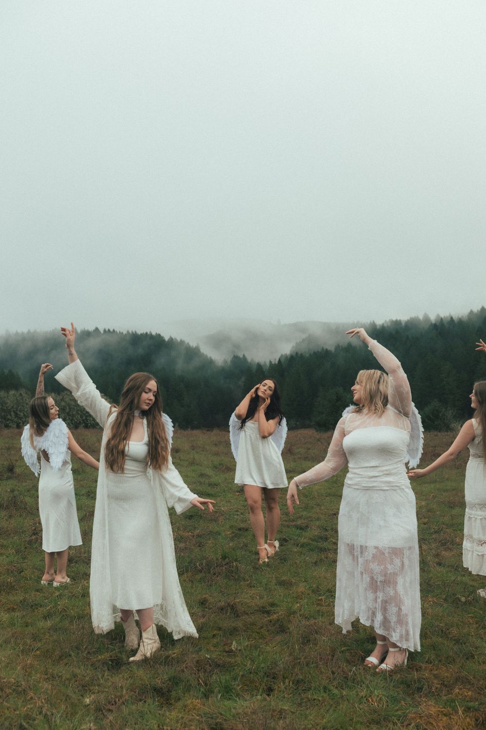 Women in white dresses dancing in a misty field with foggy forest backdrop.