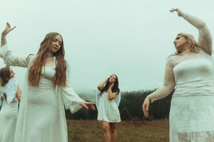 Women in white dresses dancing gracefully in an open field on a misty day.