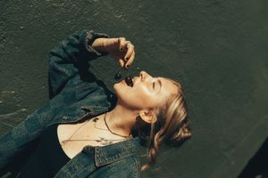 Woman in denim jacket posing against dark wall with dramatic lighting and shadows.