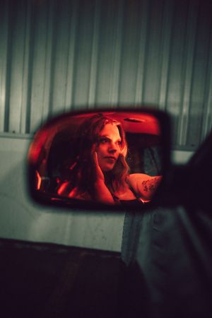 Dark moody rearview mirror reflection with red lighting creates an atmospheric nighttime scene.