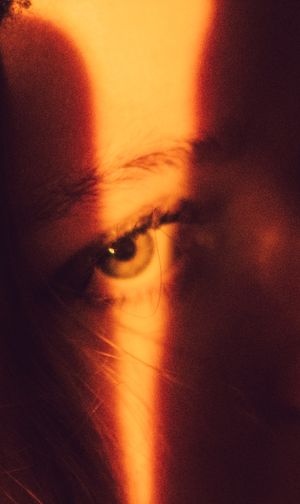 Dramatic close-up portrait with an orange light beam splitting the frame, creating a striking contrast in shadow and light.