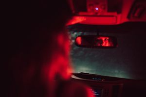 Moody red-tinted photograph of a car's interior taken from outside at night.
