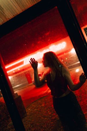 A silhouette of a person stands against a dramatic red neon light backdrop in a moody nighttime scene.