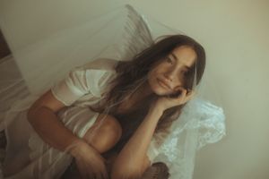 Dreamy portrait of someone resting on white bedding with soft lighting and ethereal mood.