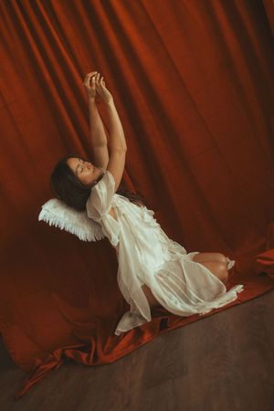 A dancer in a white dress performs an elegant movement sequence against a deep red velvet backdrop.