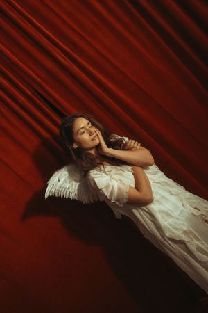 A dreamy portrait against a deep red backdrop shows a person in white reclining with ethereal lighting effects.