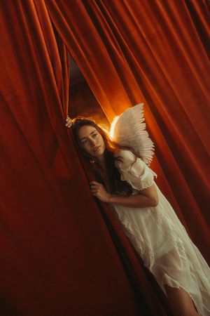 A figure in white clothing performs an ethereal dance against dramatic red curtains with theatrical lighting.