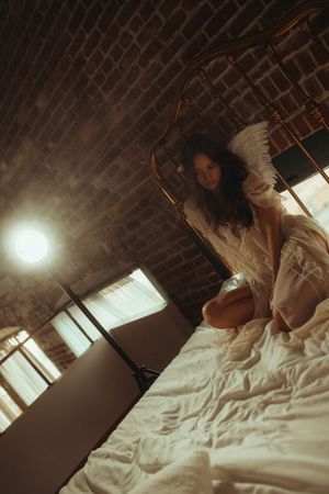 Moody boudoir photoshoot sequence with dramatic lighting and white bedding against brick wall backdrop.