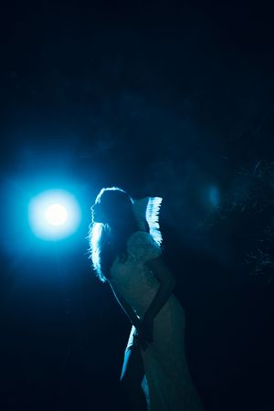 A silhouette of a figure stands against a dark background with glowing blue backlighting creating a dramatic effect.