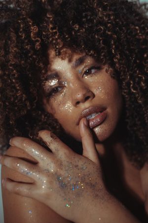 Close up beauty portrait with glitter makeup and curly natural hair in artistic lighting.