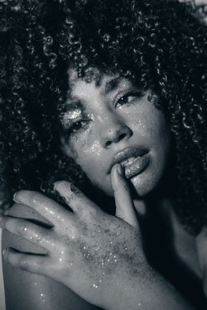 Black and white portrait with glitter details showing natural curly hair and soft expression in dramatic lighting.
